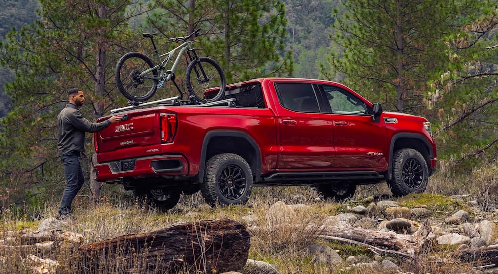 A person is loading a bike on a red 2024 GMC Sierra 1500 AT4X after leaving a GMC dealer.
