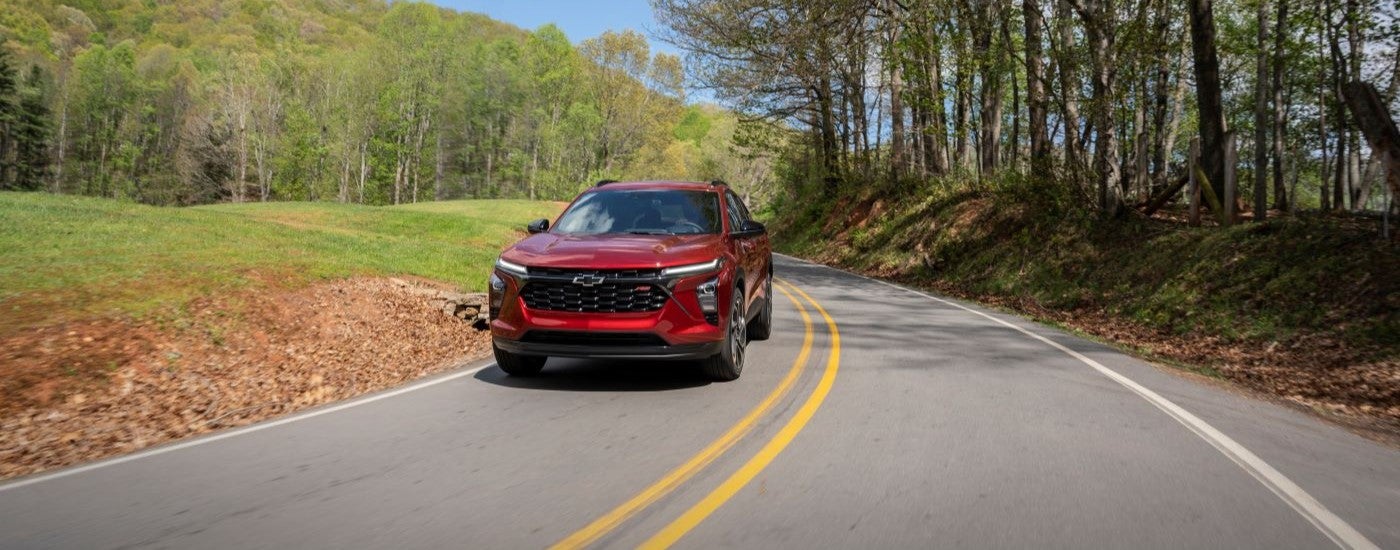 A red 2024 Chevy Trax RS shown driving a tree-lined road.