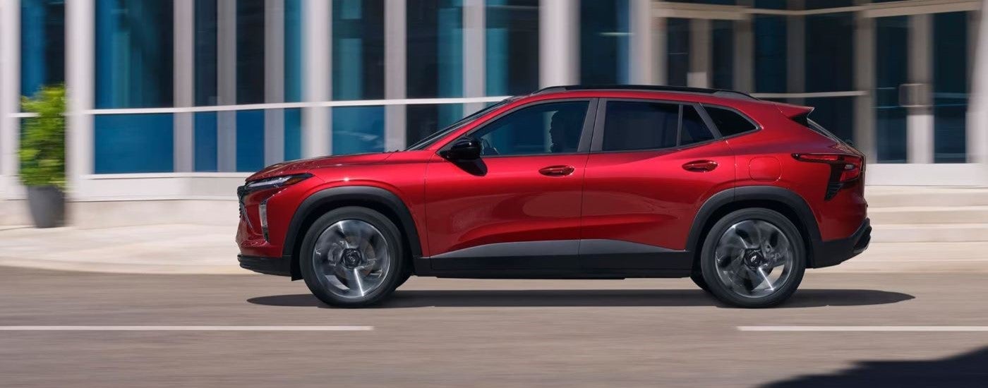 Side of a red 2024 Chevy Trax driving down a road.