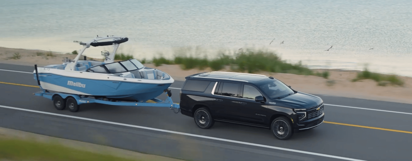 Black 2026 Chevy Suburban towing a boat along the ocean