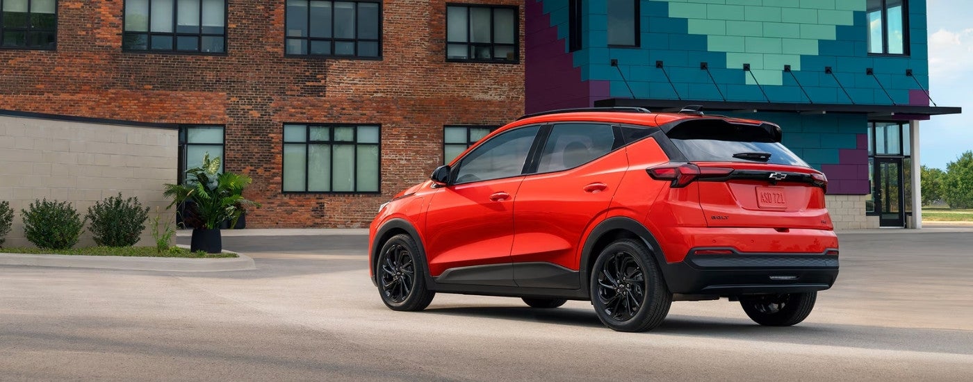 Rear of an orange 2027 Chevy Bolt parked in front of a brick building