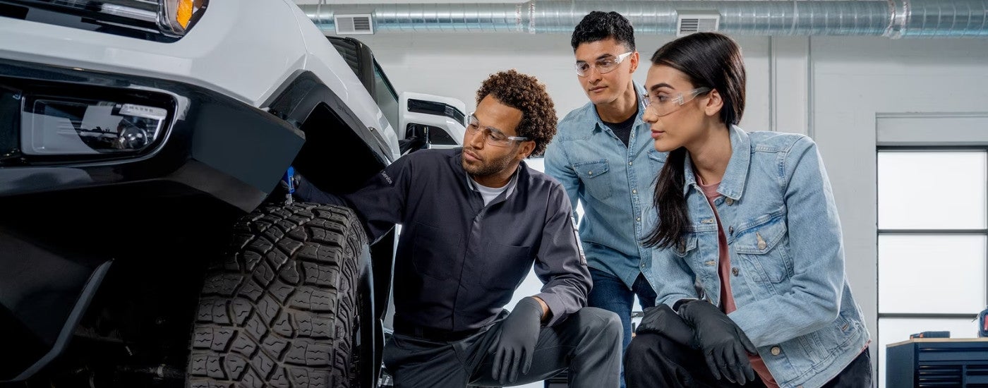 A technician is shown checking the tire tread on a white 2025 GMC Hummer EV.