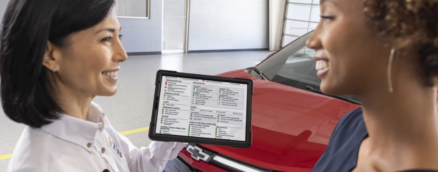 Smiling people using a tablet are shown near a red 2025 Chevy Equinox EV.