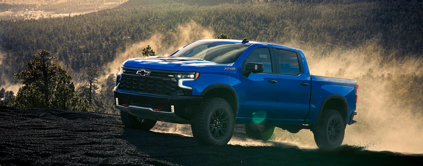 Blue 2025 Chevy Silverado 1500 driving up a dirt hill.
