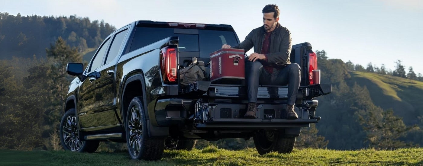 A person is using a cooler in the bed of a black 2023 GMC Sierra 1500 for sale.